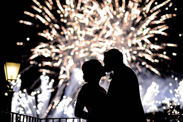 A silhouette of a man and woman kissing as white fireworks go off in the background