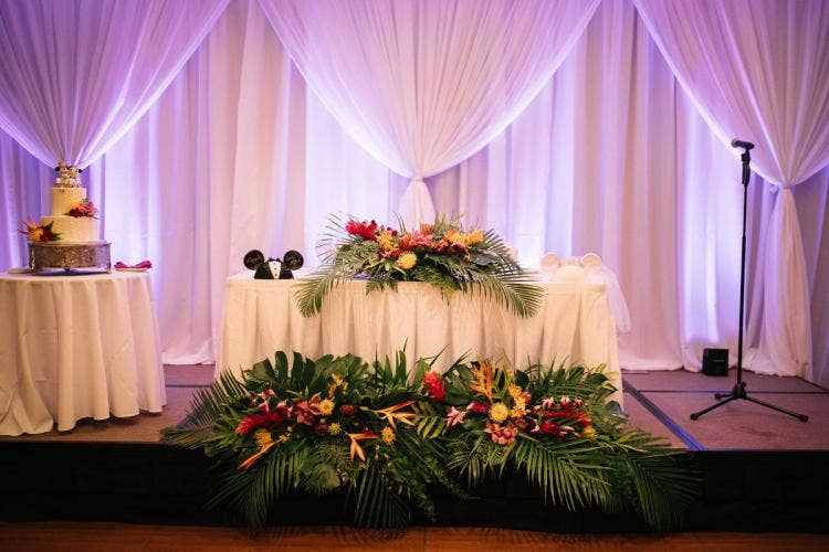 wedding reception, reception, sweetheart table, table, table decor, table floral, tropical, tropical floral, white drape, drapery wall, custom up lighting, table floral, table decor