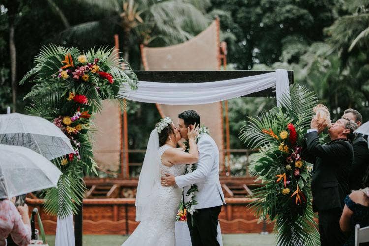 bride and groom, couple, wedding ceremony, ceremony altar area, first kiss, kiss, altar decor, altar floral, tropical floral, tropical, altar arch, white drape, aulani, halawai lawn, halawai
