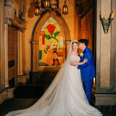 A wedding couple posing near a mural of Beauty and the Beast at Magic Kingdom Park