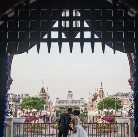 A bride and groom pose beneath a wrought iron gate at Cinderella Castle at Walt Disney World Resort