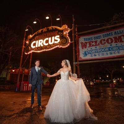 A wedding couple holding hands while posing near the Storybook Circus sign at Magic Kingdom Park