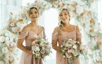 Two bridesmaids smiling and holding floral bouquets in their hands