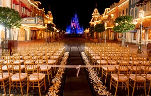 An evening wedding ceremony venue with bamboo chairs and a flower petal lined aisle, set on Main Street USA with Cinderella Castle in the background