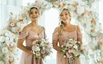 Two bridesmaids smiling and holding floral bouquets in their hands