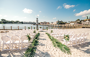 A beach with two sections of chairs facing a round table near a lighthouse