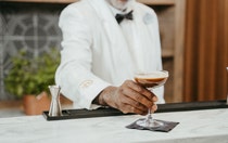 A bartender in a bowtie placing an espresso martini on a napkin atop a marble counter