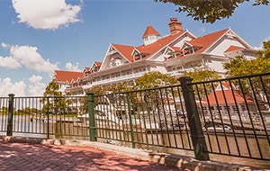 A shady brick path with a cast iron guardrail and old fashioned streetlamps looks out to the Seven Seas Lagoon and Disney's Grand Floridian Resort & Spa
