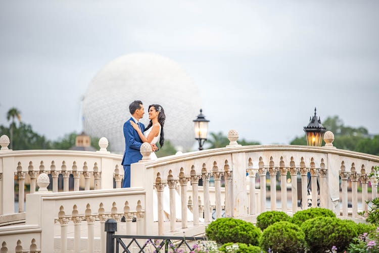 A bride and groom hugging on a bridge near Spaceship Earth at Epcot