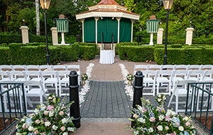 Chairs set up at a wedding venue in a garden with hedges, a canopy and floral arrangements at United Kingdom Courtyard
