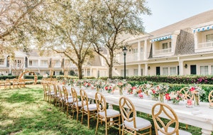 A garden venue decorated for a wedding reception with a long table, chairs and flowers in vases at Poolside Green at Disney’s BoardWalk Inn
