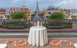 A wedding ceremony venue on a train station platform with arranged flower petals and a linen covered table with candles, overlooking Main Street USA and Cinderella Castle