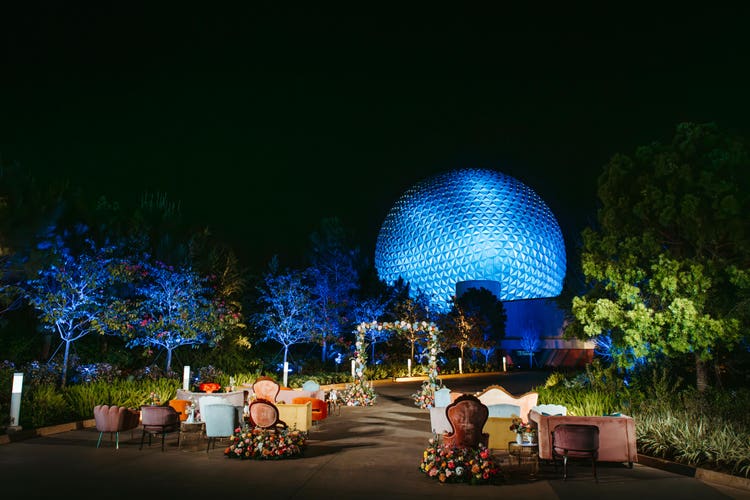 Eclectic velvet chairs and sofas, a tree lined path, a floral wedding arch and an illuminated Spaceship Earth