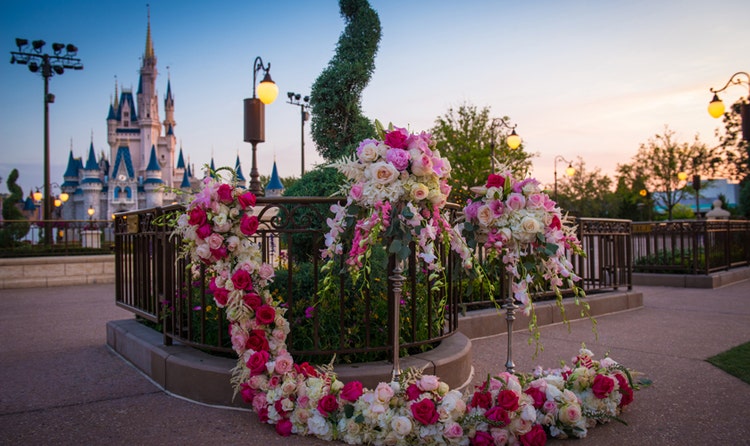 Cinderella's Castle stands in the background of a wrought iron railing decorated with floral arrangements