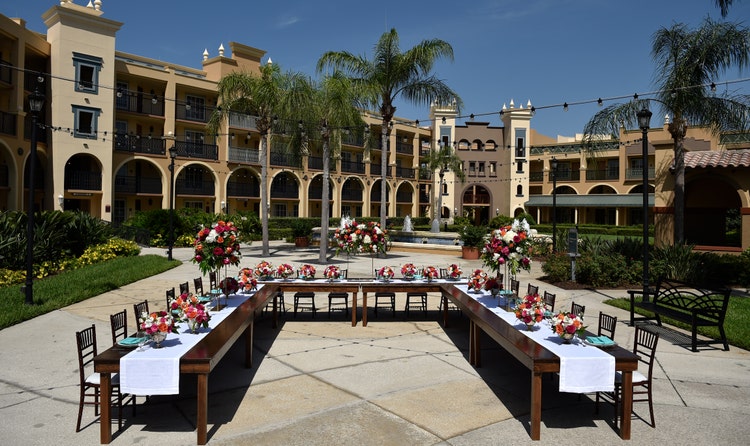 Three large tables arranged in a U shape surrounded by palm trees and a water fountain