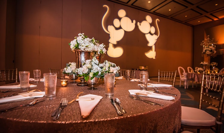 A roundtable table with floral centerpieces near a projection of Mickey and Minnie kissing