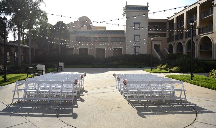 Two sections of chairs arranged in rows in a courtyard under lights stringing from side to the other