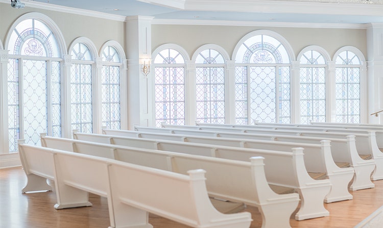 A section of pews and a wall of arched, stained-glass windows in a chapel at Disney’s Wedding Pavilion