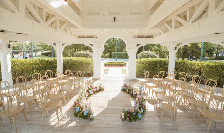 A wedding ceremony venue in a gazebo at Seabreeze Point with bentwood chairs and rose and hydrangea floral arrangements lining the aisle