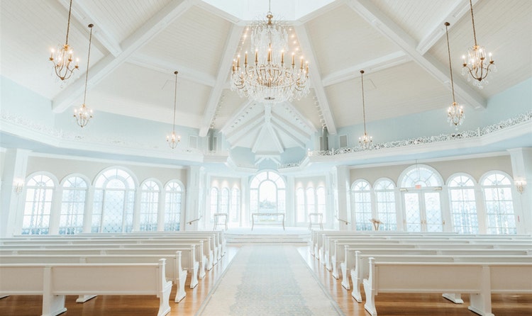 A vaulted ceiling with crystal chandeliers above an aisle and 2 rows of pews leading to an elegant altar