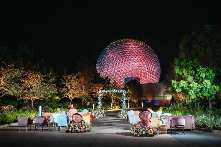 Rows of eclectic velvet chairs and sofas, an ornate floral wedding arch and an illuminated Spaceship Earth