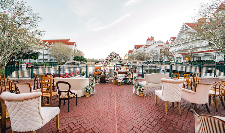 The patio at Disney’s Grand Floridian Resort and Spa, overlooking the marina, with chairs and love seats facing a floral wedding arch