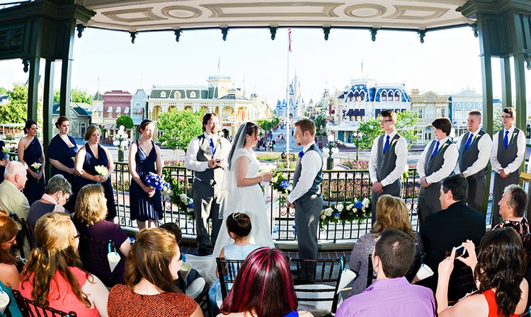 A bride and groom stand with their wedding party on a balcony overlooking Main Street USA