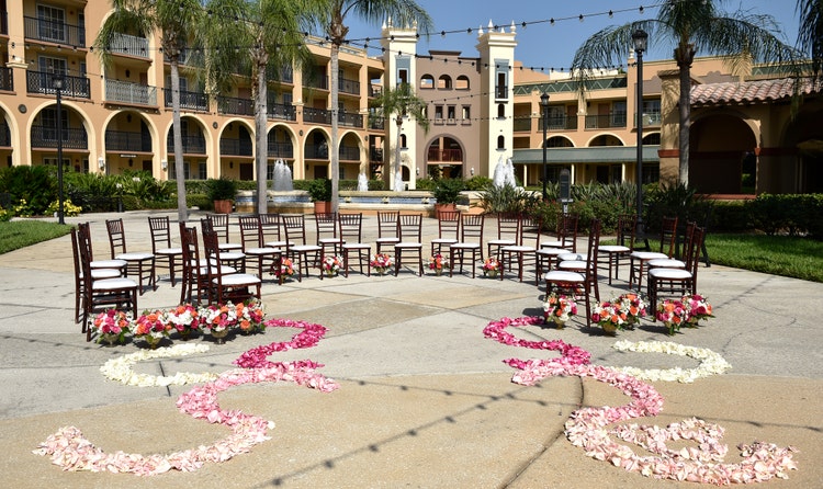 Rose petals lead to a group of chairs arranged in a semi circle on a courtyard with a large water fountain