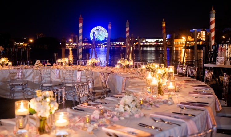 A wedding reception’s table settings with Spaceship Earth lit up in the background at night