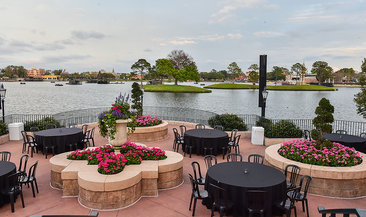 Several tables and chairs and 3 flower beds at Terrace des Fleurs, a large terrace overlooking Crescent Lake at EPCOT