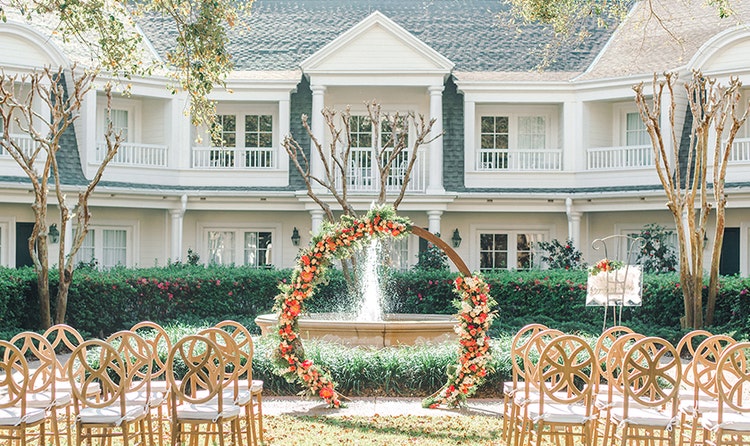 A garden venue decorated for a wedding ceremony with a floral arch at Poolside Green at Disney’s BoardWalk Inn