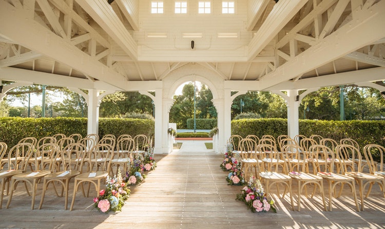 A wedding ceremony venue in a gazebo at Seabreeze Point with bentwood chairs and rose and hydrangea floral arrangements lining the aisle