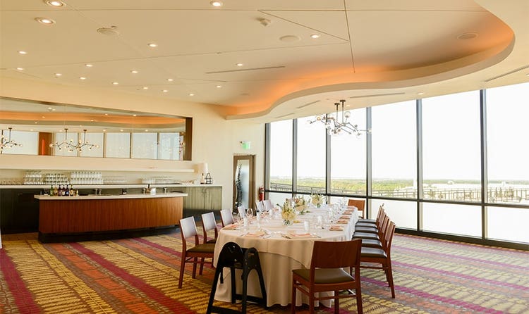 A long table surrounded by many chairs next to a bar