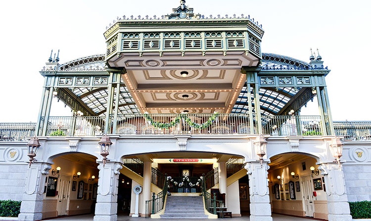 A staircase leads up to a second floor balcony at a train station