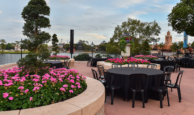 Several tables and chairs arranged between the flower beds at Terrace des Fleurs, a large terrace overlooking Crescent Lake at EPCOT