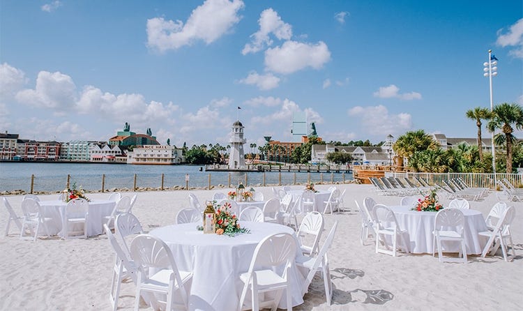 Several round tables on a beach near a dock and a lighthouse