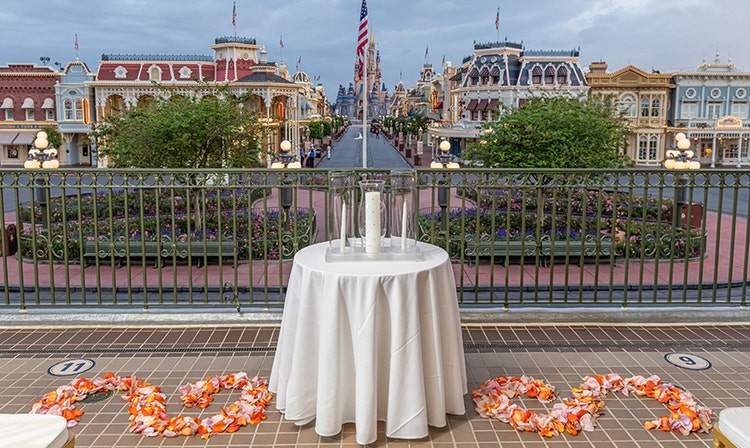 A wedding ceremony venue on a train station platform with arranged flower petals and a table with candles, overlooking Main Street USA and Cinderella Castle