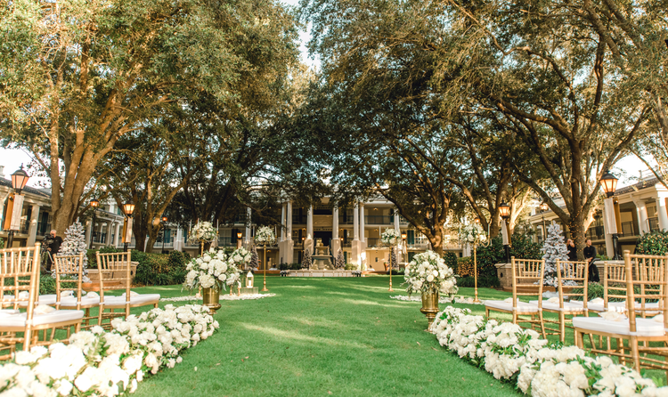 Chairs set up on a lawn with flower bouquets surrounded by oak trees facing Oak Manor in Disney’s Port Orleans Riverside