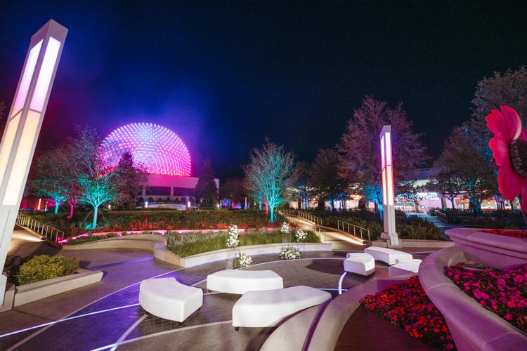 Geometric benches in a pavilion, trees with backlighting and a pathway leading to Spaceship Earth at Epcot
