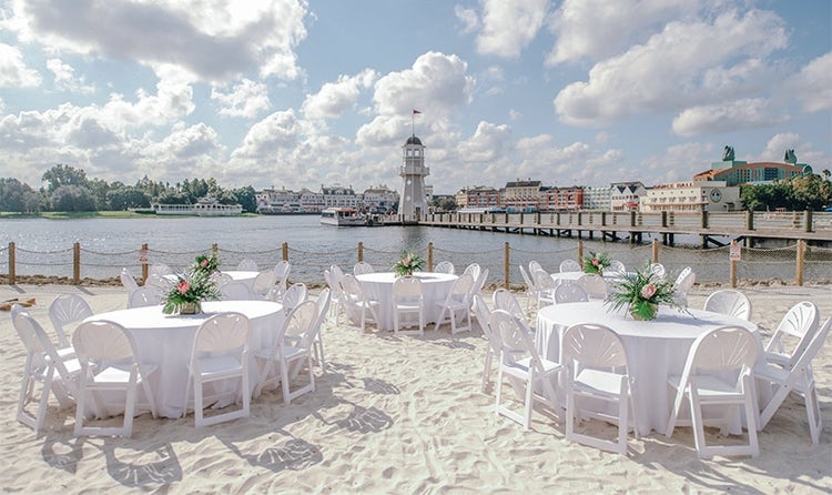 Several round tables on a beach near a dock and a lighthouse
