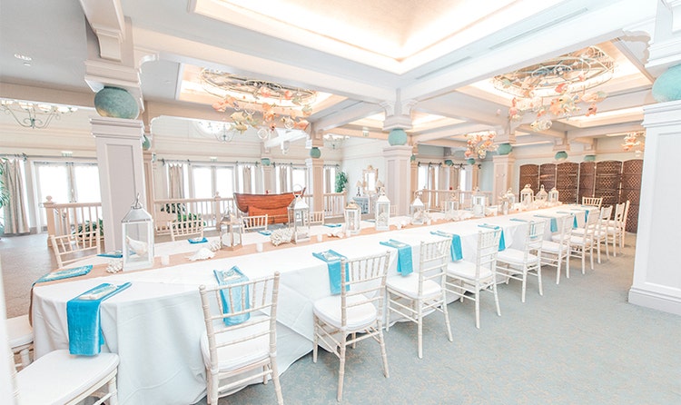 Several chairs around a long table decorated with seashells and lanterns under ornate hanging decorations