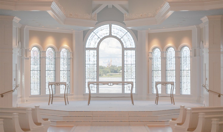 An altar with 3 tables and a view of Cinderella Castle through arched, stained-glass windows at Disney’s Wedding Pavilion