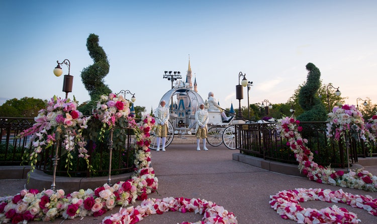 A wedding venue decorated with flowers exits to 2 footmen standing next to the Cinderella Carriage in front of Cinderella's Castle