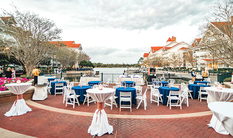 The patio at Disney’s Grand Floridian Resort and Spa, overlooking the marina, with many small tables covered with tablecloths, and folding chairs around the tables