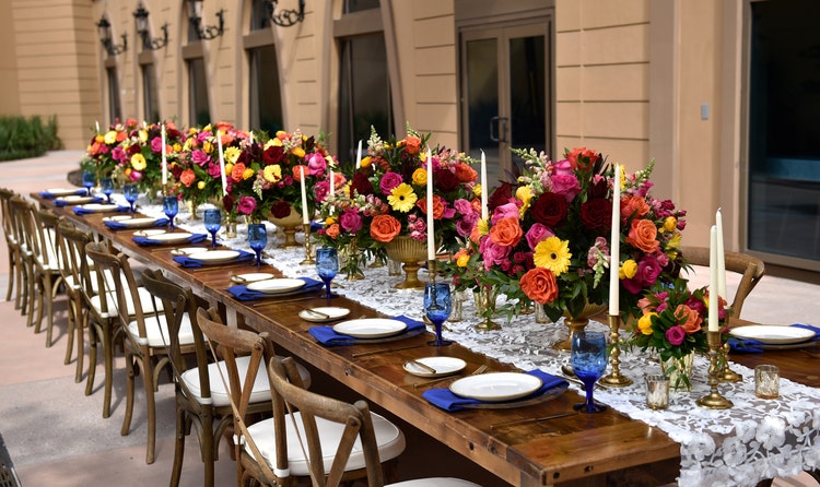 A lace runner extends down a long table holding several large floral centerpieces and tall candlesticks