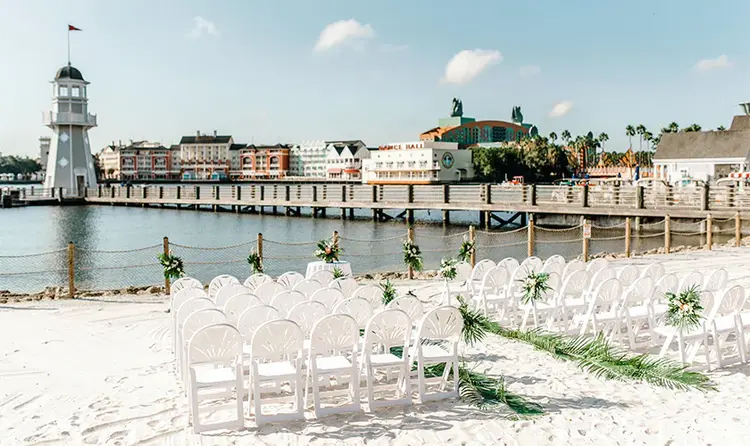 Five tables surrounded by chairs on a beach near a cluster of palm trees