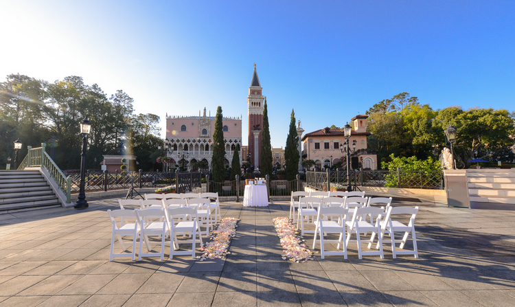 An aisle lined with flower petals and chairs, leading to a wedding altar and quaint church buildings