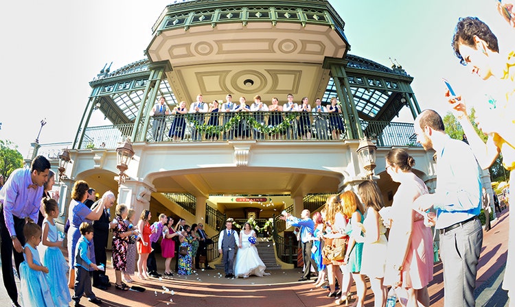 People throw flower petals at the bride and groom as they emerge from the Train Station at Magic Kingdom park