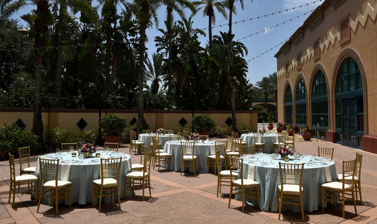 Five circular tables with chairs arranged in a courtyard surrounded by plants