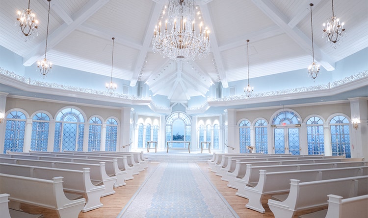 A chapel and altar in Disney’s Wedding Pavilion with several chandeliers, a wide aisle and 2 sides of pews